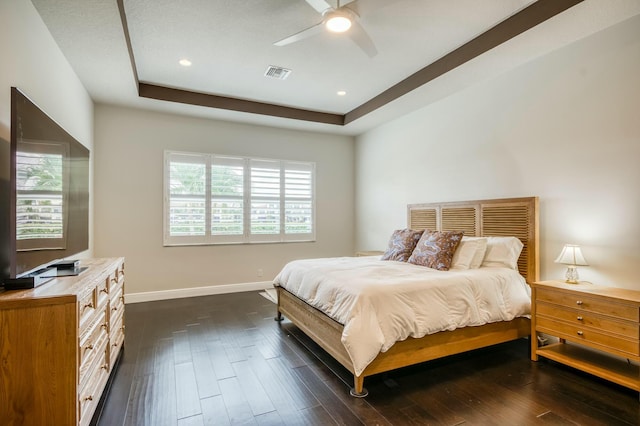 bedroom with ceiling fan, dark wood-type flooring, a tray ceiling, and multiple windows