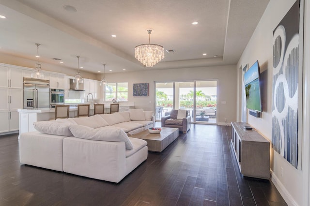 living room featuring dark wood-type flooring, a raised ceiling, and a notable chandelier