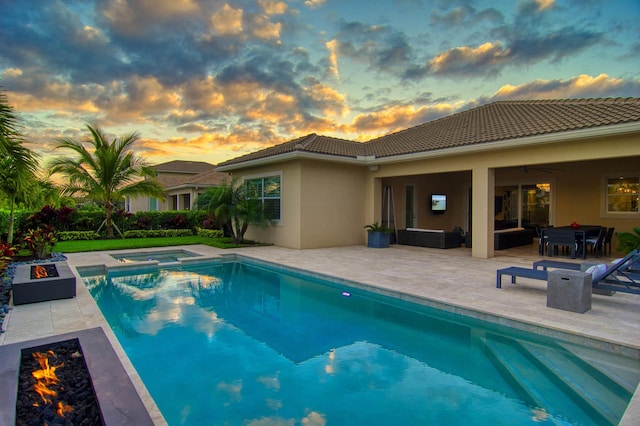 pool at dusk featuring ceiling fan, an outdoor living space with a fire pit, a patio area, and an in ground hot tub