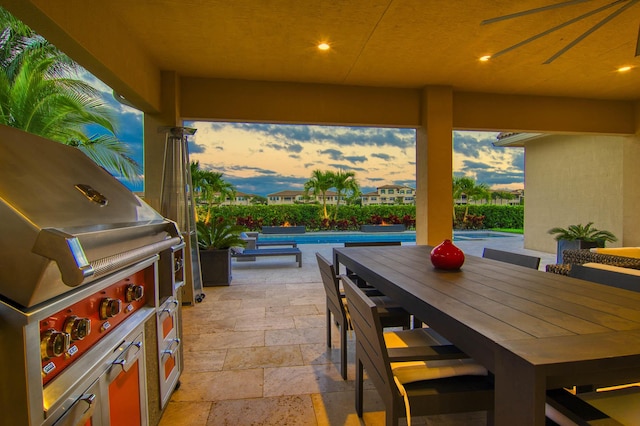 patio terrace at dusk featuring ceiling fan and an outdoor kitchen