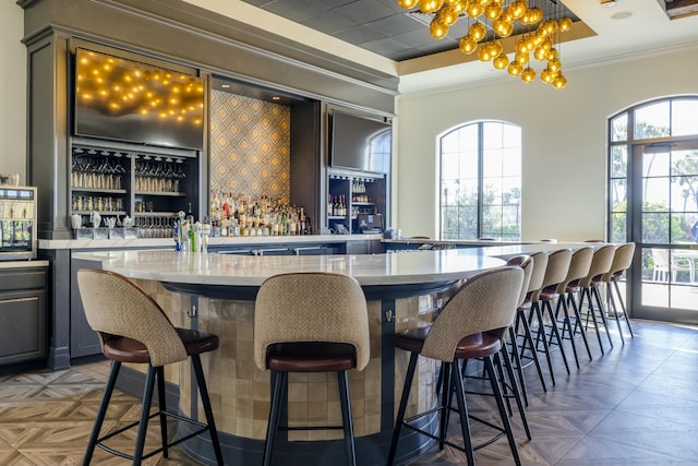 bar with ornamental molding, a chandelier, dark parquet flooring, and light stone countertops