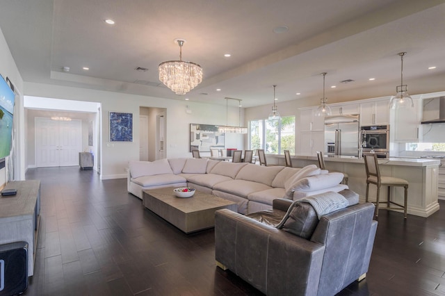 living room with an inviting chandelier, a raised ceiling, and dark hardwood / wood-style floors