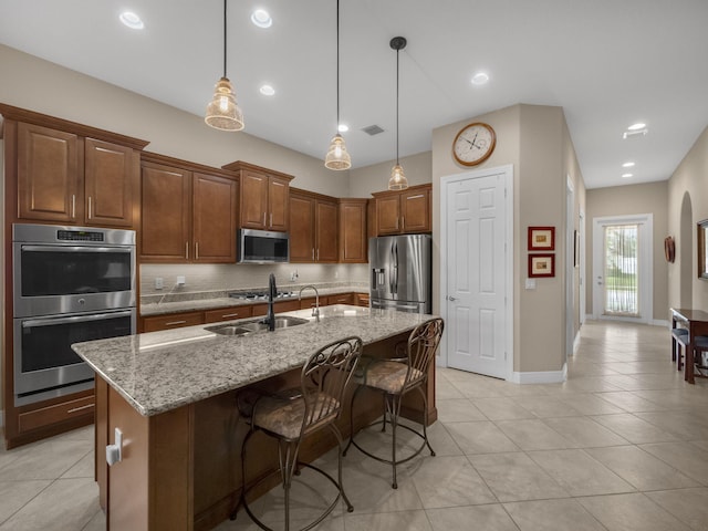 kitchen featuring light stone counters, hanging light fixtures, a center island with sink, a breakfast bar, and appliances with stainless steel finishes