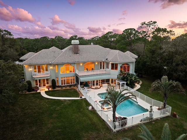 back house at dusk featuring a yard, a balcony, a patio, and a fenced in pool