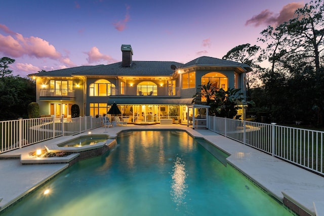 pool at dusk with outdoor lounge area, an in ground hot tub, and a patio