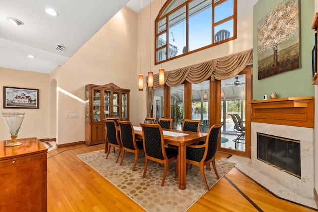 dining area with a high end fireplace, light hardwood / wood-style floors, and high vaulted ceiling