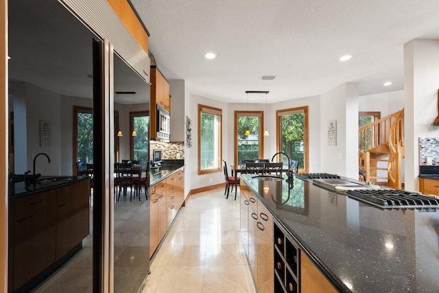 kitchen with backsplash, stainless steel appliances, sink, pendant lighting, and dark stone countertops