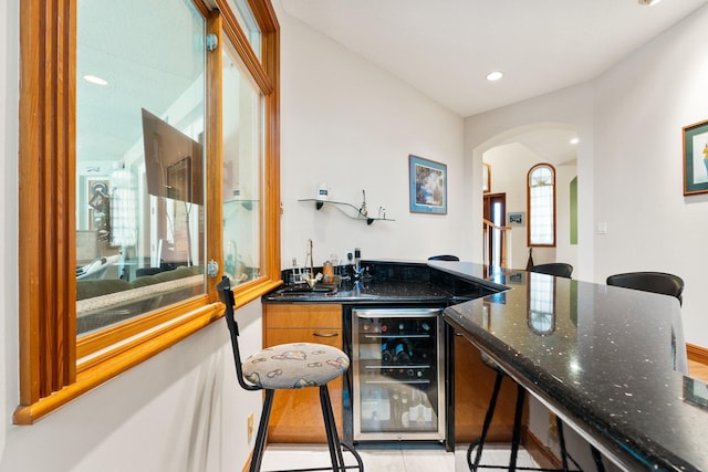 bar with light tile patterned floors, beverage cooler, and dark stone countertops