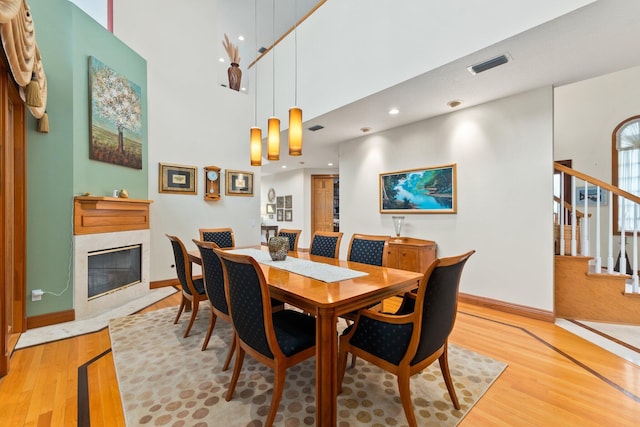 dining area with light wood-type flooring, a high ceiling, and a high end fireplace