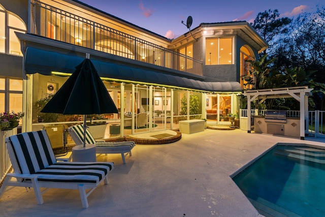 back house at dusk featuring a pergola, a balcony, a patio area, and exterior kitchen