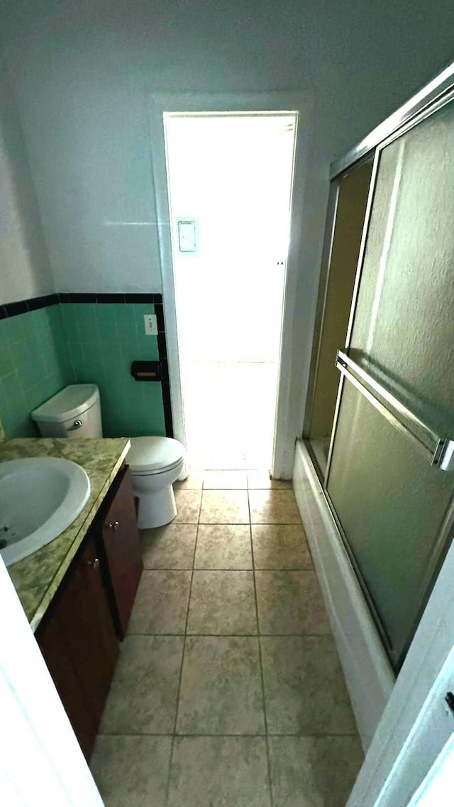 full bathroom with tile patterned flooring, combined bath / shower with glass door, toilet, vanity, and tile walls