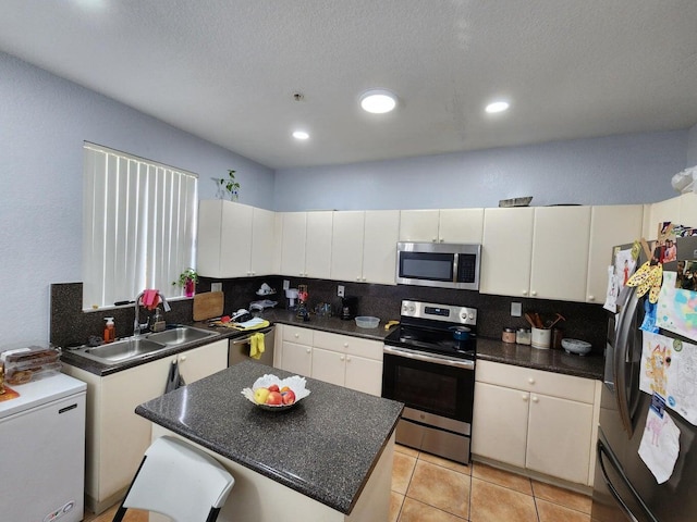 kitchen with stainless steel appliances, sink, light tile patterned floors, white cabinets, and a kitchen island