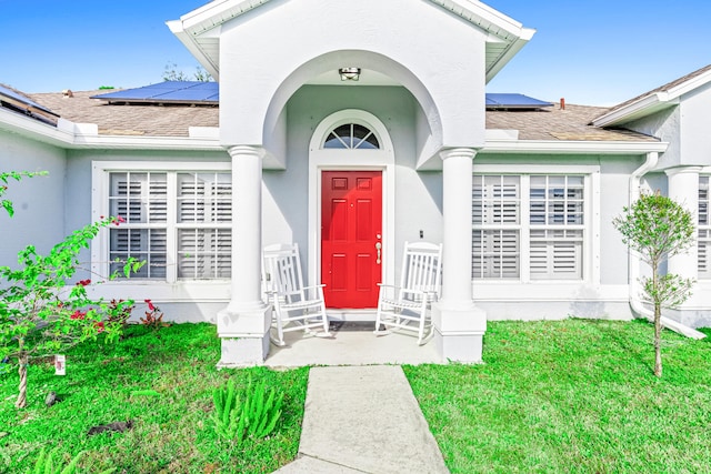 view of exterior entry with solar panels and a lawn