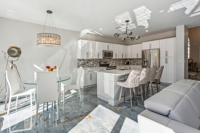 kitchen with white cabinetry, a kitchen island with sink, pendant lighting, and appliances with stainless steel finishes