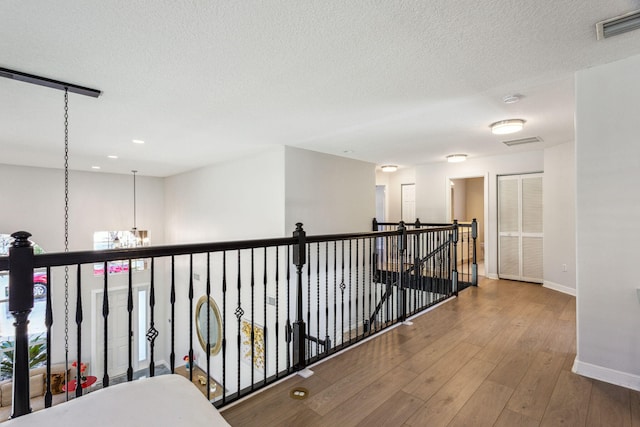 corridor featuring hardwood / wood-style floors, a textured ceiling, and a chandelier