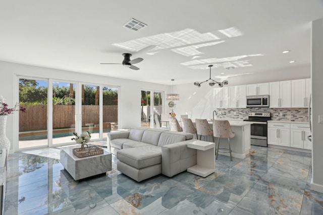 living room with ceiling fan with notable chandelier, sink, and a wealth of natural light