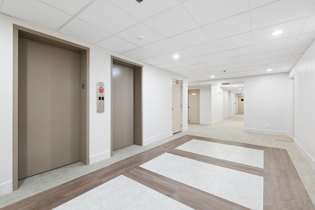 hall featuring a drop ceiling, light wood-type flooring, and elevator