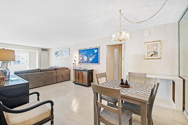 dining room with a textured ceiling, light hardwood / wood-style floors, and an inviting chandelier