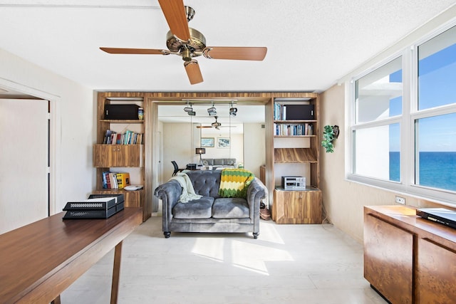 living room featuring ceiling fan, a water view, and a textured ceiling