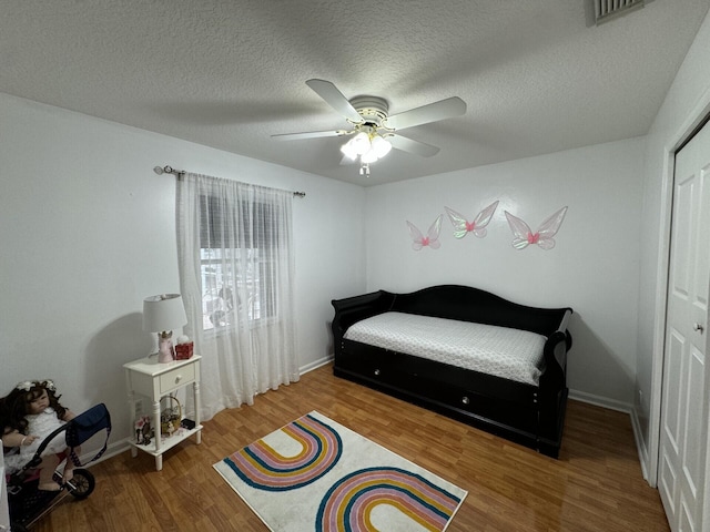 bedroom with wood-type flooring, a textured ceiling, ceiling fan, and a closet