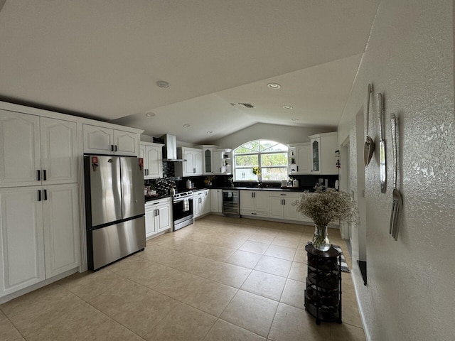 kitchen featuring wall chimney range hood, appliances with stainless steel finishes, white cabinets, vaulted ceiling, and beverage cooler