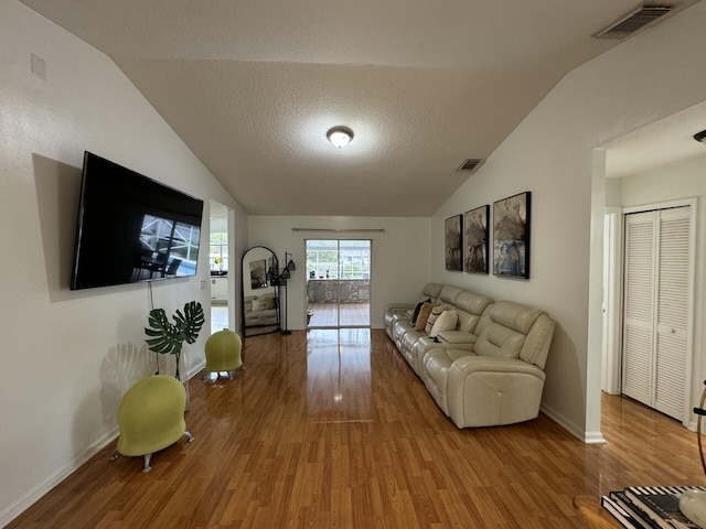 living room with a textured ceiling, hardwood / wood-style floors, and vaulted ceiling