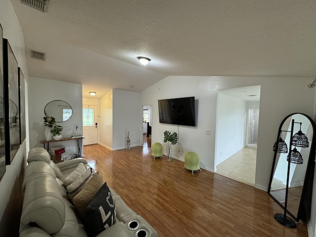 living room with vaulted ceiling, a textured ceiling, and light wood-type flooring