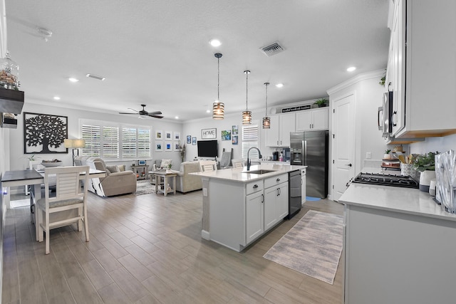 kitchen featuring white cabinetry, sink, hanging light fixtures, stainless steel fridge with ice dispenser, and a kitchen island with sink