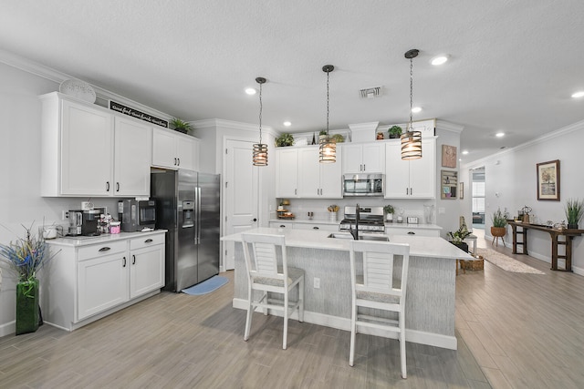 kitchen featuring appliances with stainless steel finishes, crown molding, pendant lighting, white cabinets, and an island with sink