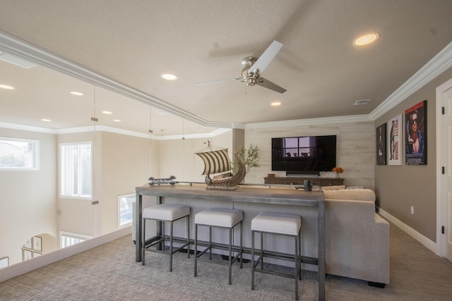 interior space featuring a breakfast bar area, ceiling fan, carpet, and crown molding