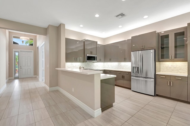 kitchen featuring kitchen peninsula, appliances with stainless steel finishes, decorative backsplash, gray cabinetry, and light tile patterned flooring