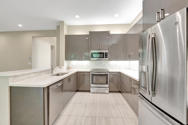 kitchen with kitchen peninsula, backsplash, gray cabinetry, stainless steel appliances, and sink