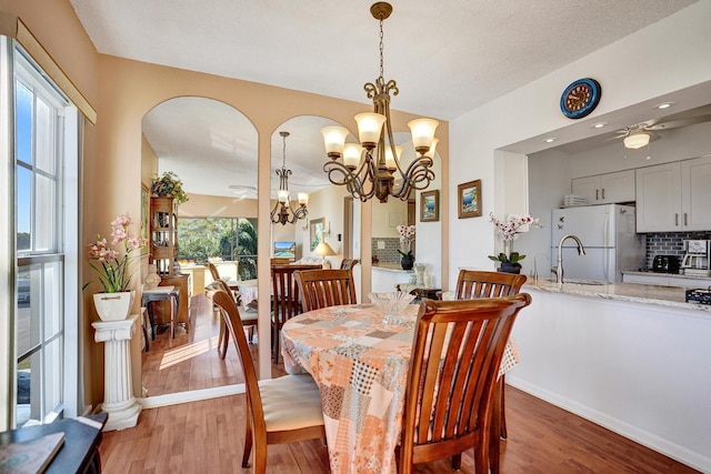 dining room with light wood-style floors, arched walkways, an inviting chandelier, and baseboards