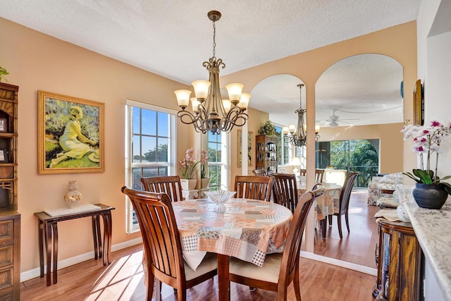 dining space featuring a textured ceiling, arched walkways, baseboards, ceiling fan with notable chandelier, and light wood-style flooring