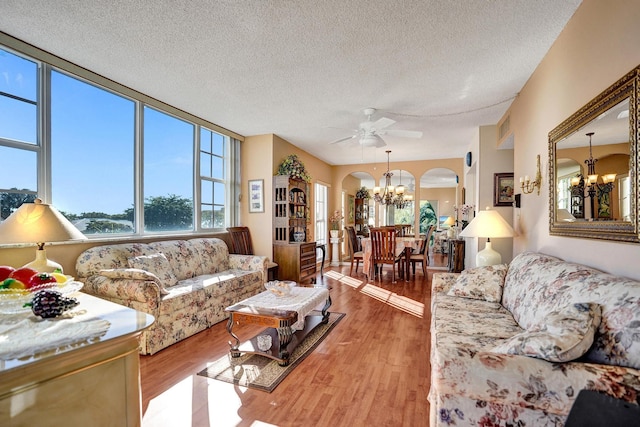 living area featuring light wood-style floors, visible vents, arched walkways, and ceiling fan with notable chandelier