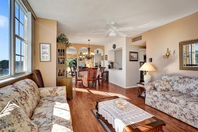 living room with a textured ceiling, ceiling fan with notable chandelier, wood finished floors, visible vents, and baseboards