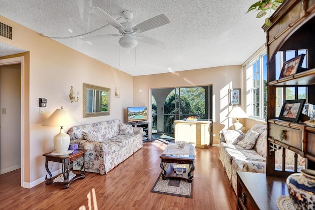 living area with ceiling fan, a textured ceiling, baseboards, and wood finished floors