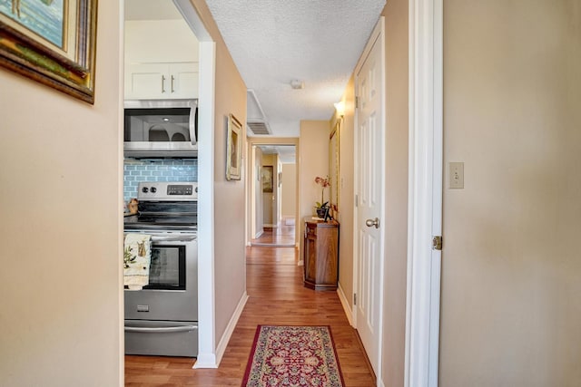 hall with visible vents, a textured ceiling, baseboards, and wood finished floors