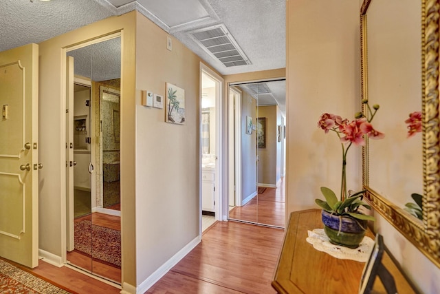 corridor with a textured ceiling, baseboards, wood finished floors, and visible vents