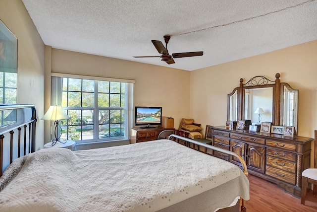 bedroom with a ceiling fan, a textured ceiling, wood finished floors, and multiple windows
