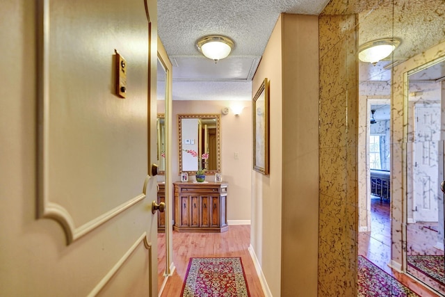 corridor featuring a textured ceiling, wood finished floors, and baseboards