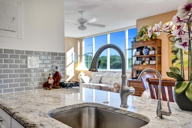 room details with ceiling fan, light stone counters, a sink, and decorative backsplash