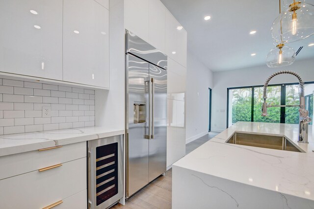 kitchen with wine cooler, stainless steel built in fridge, light stone counters, and sink