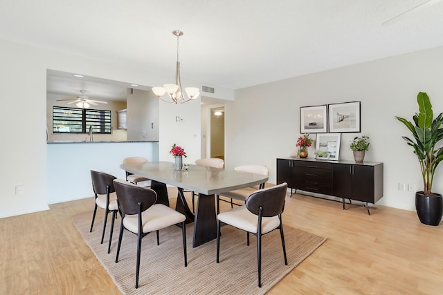 dining space with ceiling fan with notable chandelier, sink, and light hardwood / wood-style floors