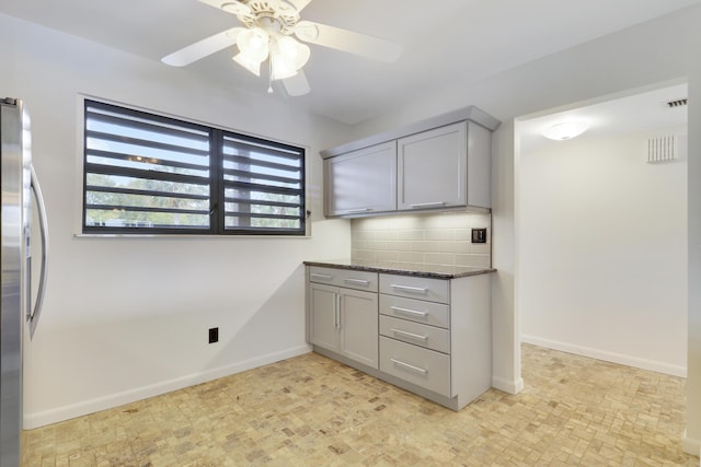 kitchen featuring gray cabinets, stainless steel refrigerator, ceiling fan, tasteful backsplash, and dark stone counters