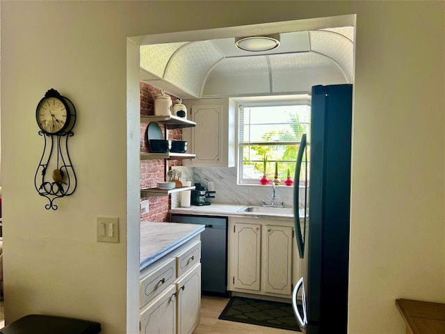 kitchen featuring backsplash, sink, fridge, and black dishwasher