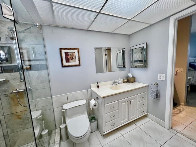 bathroom featuring vanity, toilet, a shower with door, and tile walls