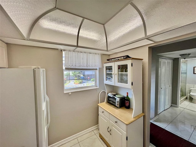 kitchen featuring white cabinets, white fridge, and light tile patterned flooring