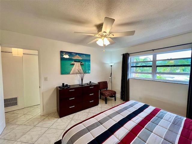 tiled bedroom with ceiling fan and a textured ceiling