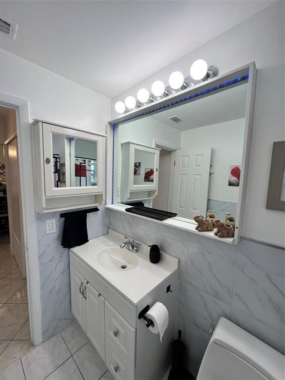 bathroom featuring tile patterned floors, vanity, toilet, and tile walls